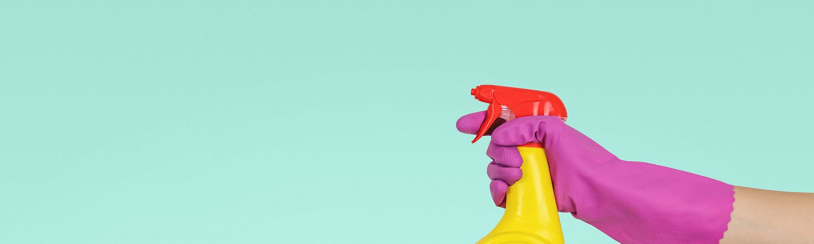 A hand wearing a rubber glove holds a spray bottle.