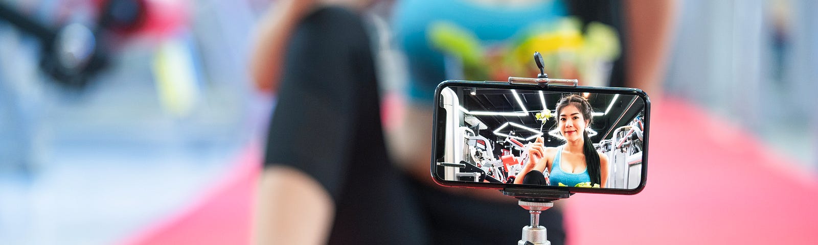 A photo of a woman recording herself doing a workout using her smartphone on a tripod.