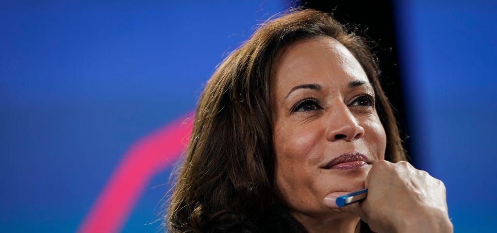 Closeup photo of Kamala Harris with a slight smile on her face, hand on chin.