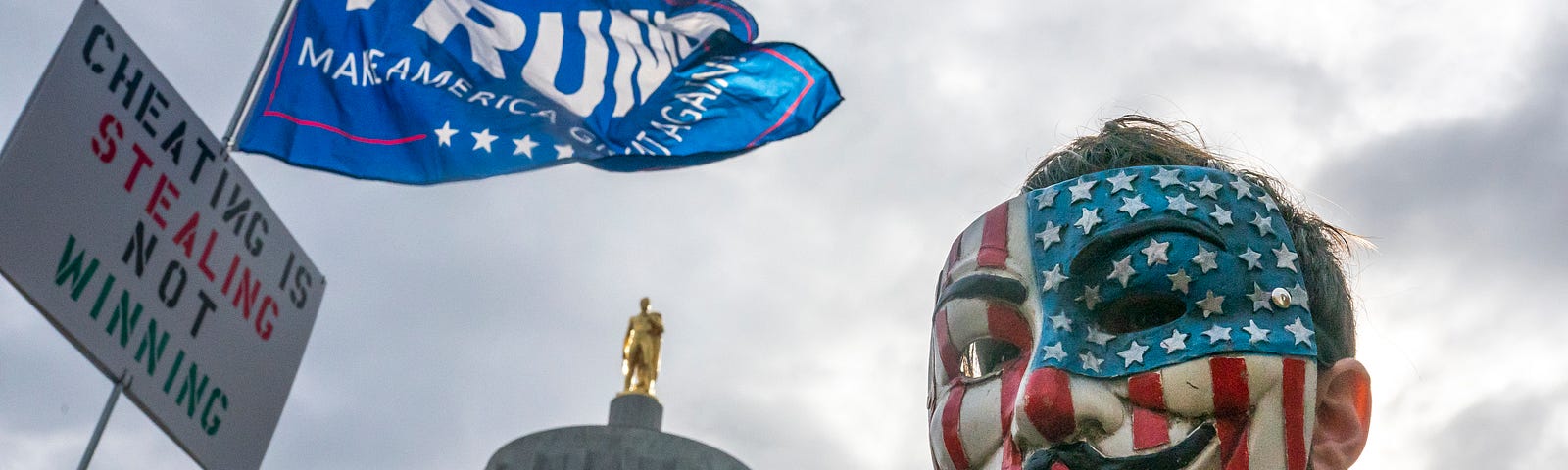 A protester in a Guy Fawkes mask stands in front of the Oregon State Capitol building during a Stop the Steal rally on Nov. 7