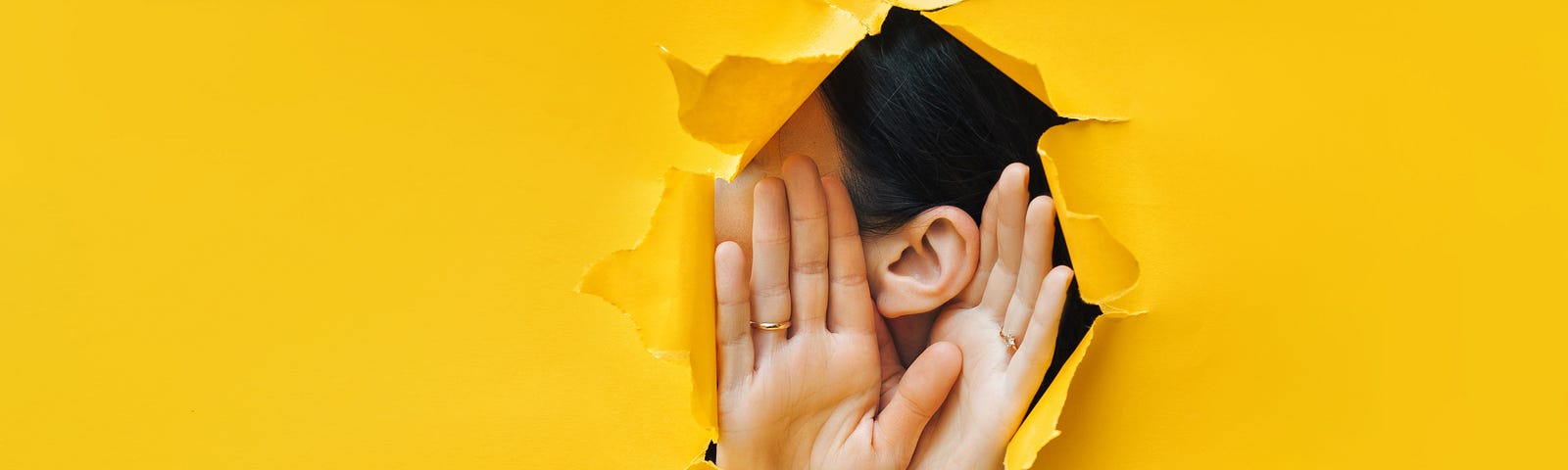 Female ear and hands close-up. Copy space. Torn paper, yellow background.