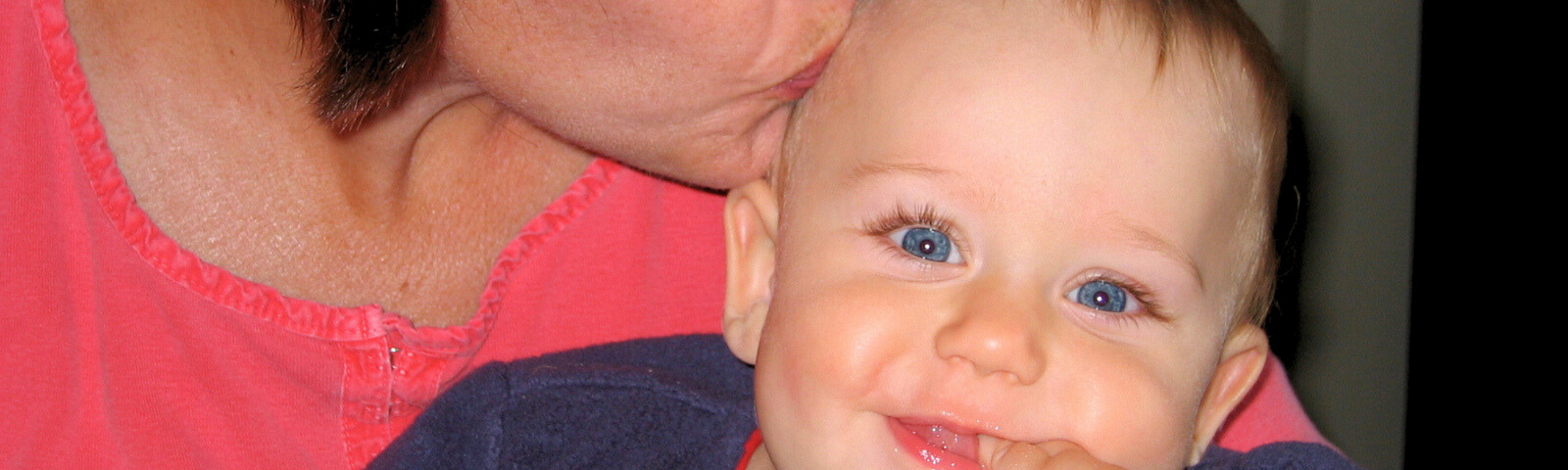 Closeup of a Mom kissing the top of her baby’s head, while baby is smiling at camera.