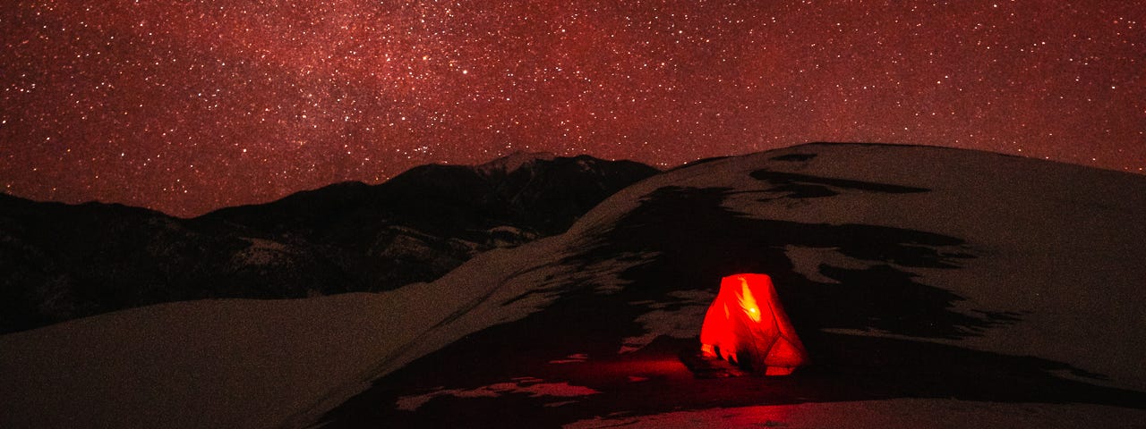 A brilliant night sky over frozen sand dunes at Great Sand Dunes National Park, with my small tent lit up in the foreground.