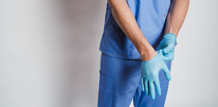 Close up of the hands of a man in blue scrubs pulling on surgical gloves