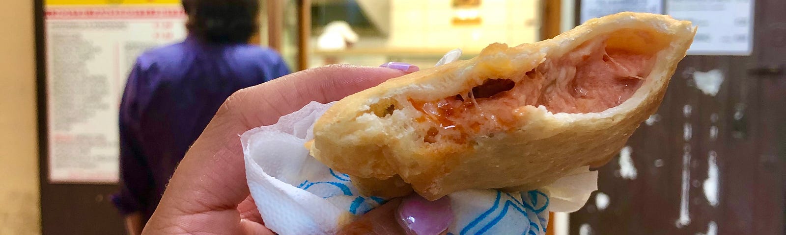 Closeup of a hand holding a half-eaten pastry, taken in front of the restaurant.