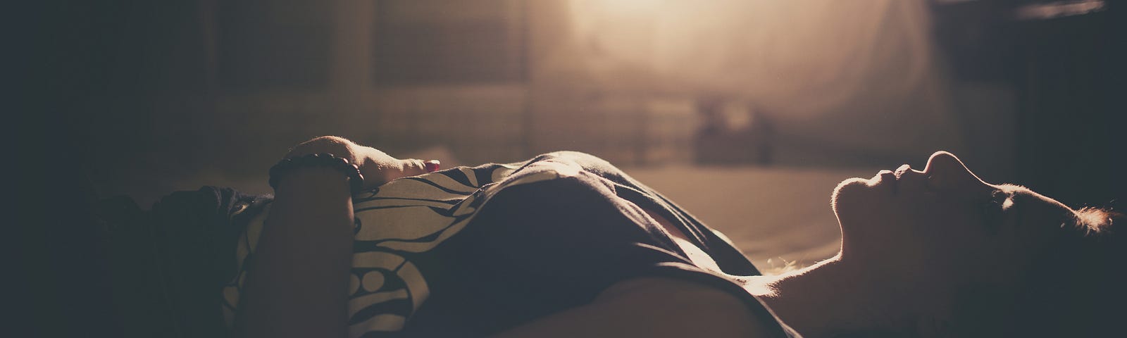 Sad girl lying down on bed as sunlight wafts in.