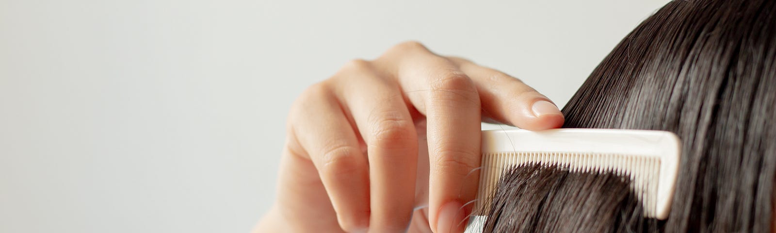 Close-up of woman combing hair against white background