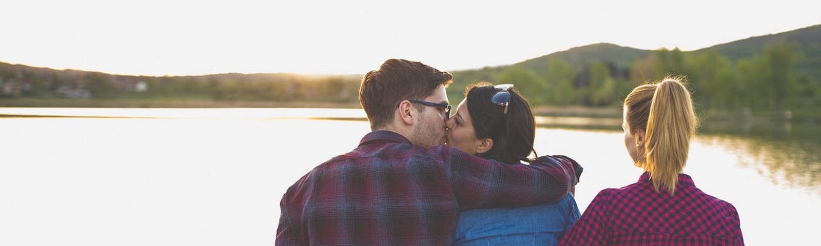 Two people kissing while one holds hands with a third person.