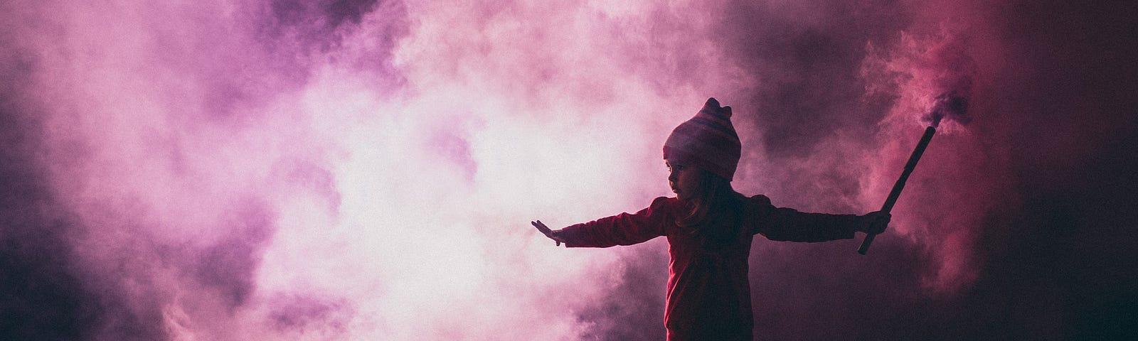 Silhouette of a young child holding a stick that’s creating pink fog