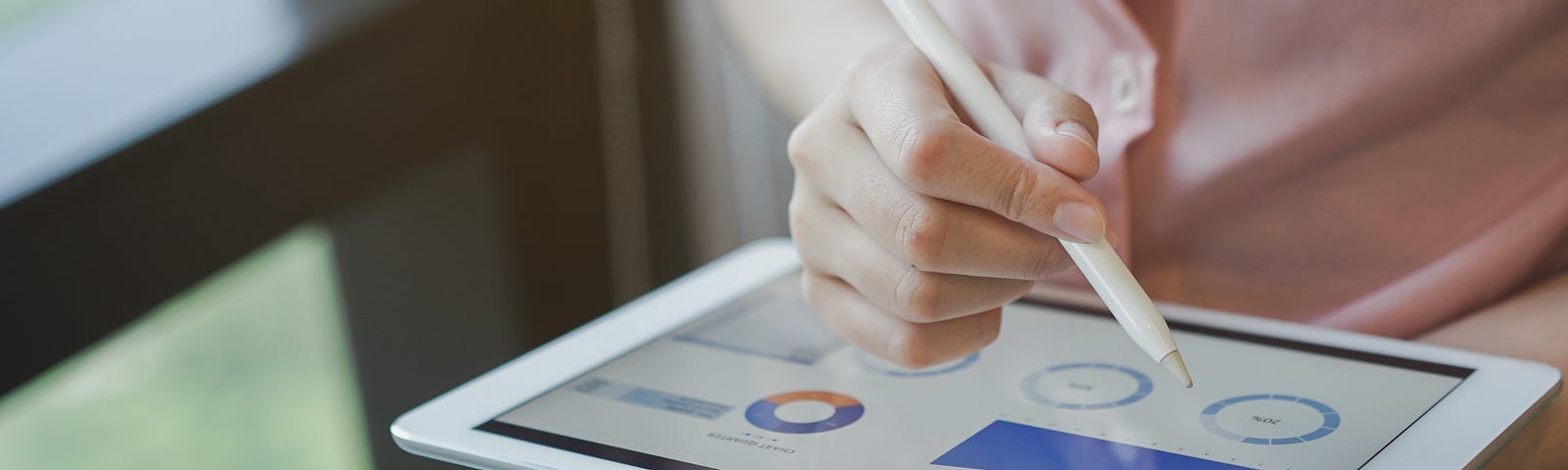 A close up on businesswoman’s hand using a stylus pen on a tablet, commenting on a metrics dashboard.