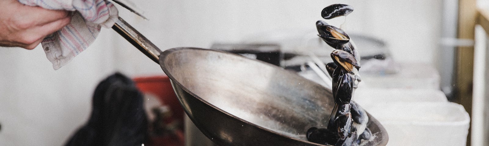 A person holding gray cooking pan and cooking clams without sticking