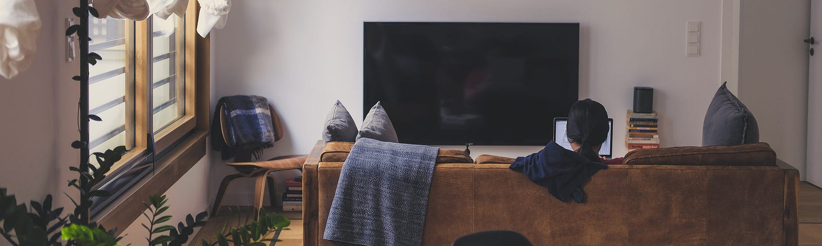 A photo taken from the rear of a person working on their laptop while sitting on the sofa.