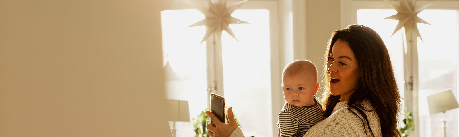 Mother holding baby son and taking a photo of something.