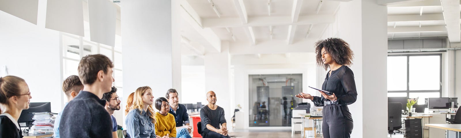 A young woman stands in front of her team and addresses them in a meeting.