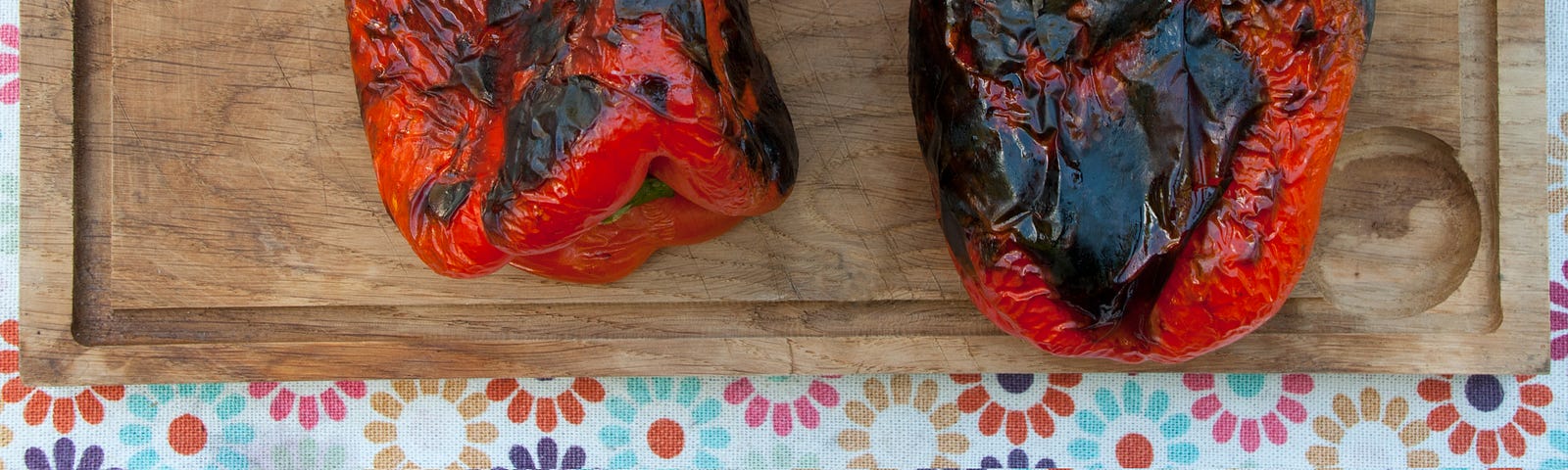 Charred red peppers on a wooden board.