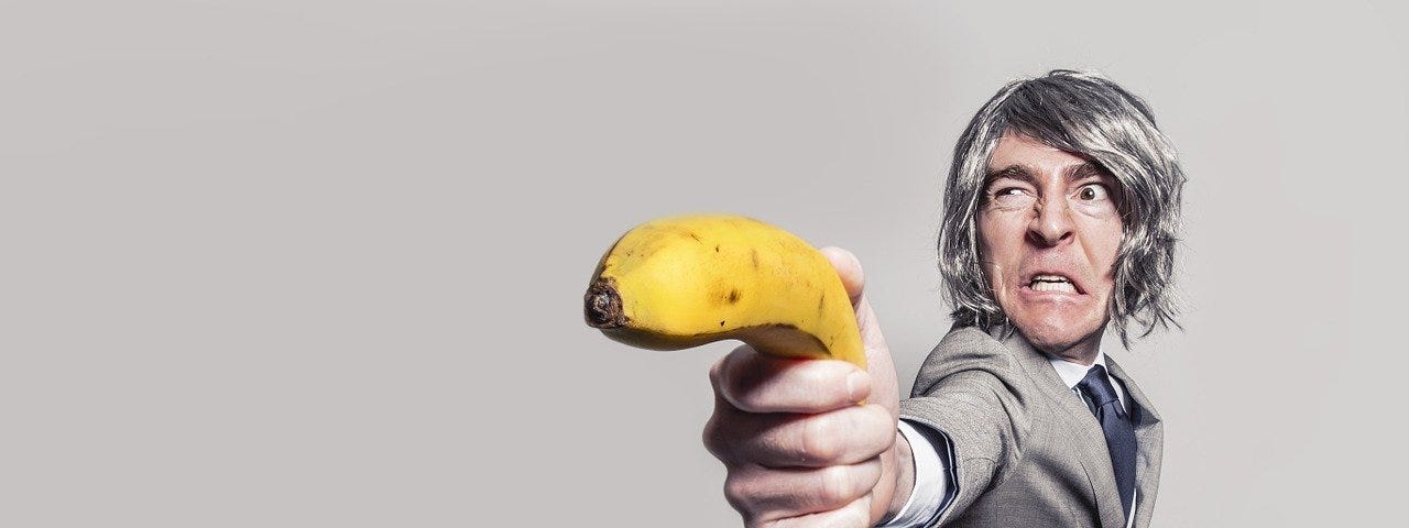 A man in suit holding a banana like a gun with funny expression on his face.