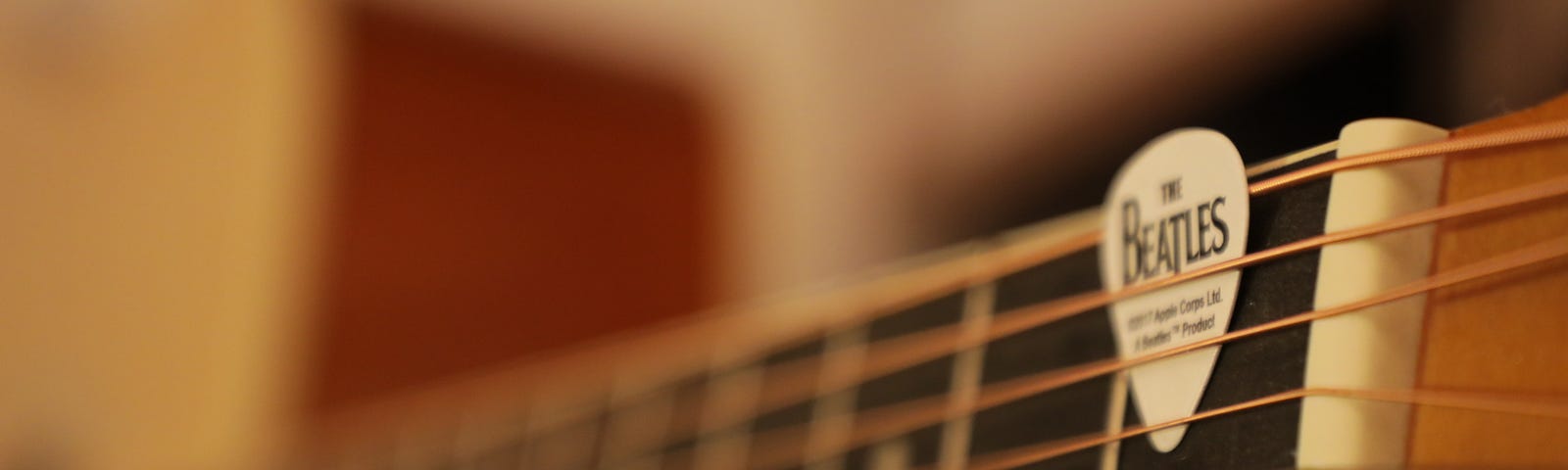 A close-up of a guitar fret board, with a pick with “The Beatles” written on it.