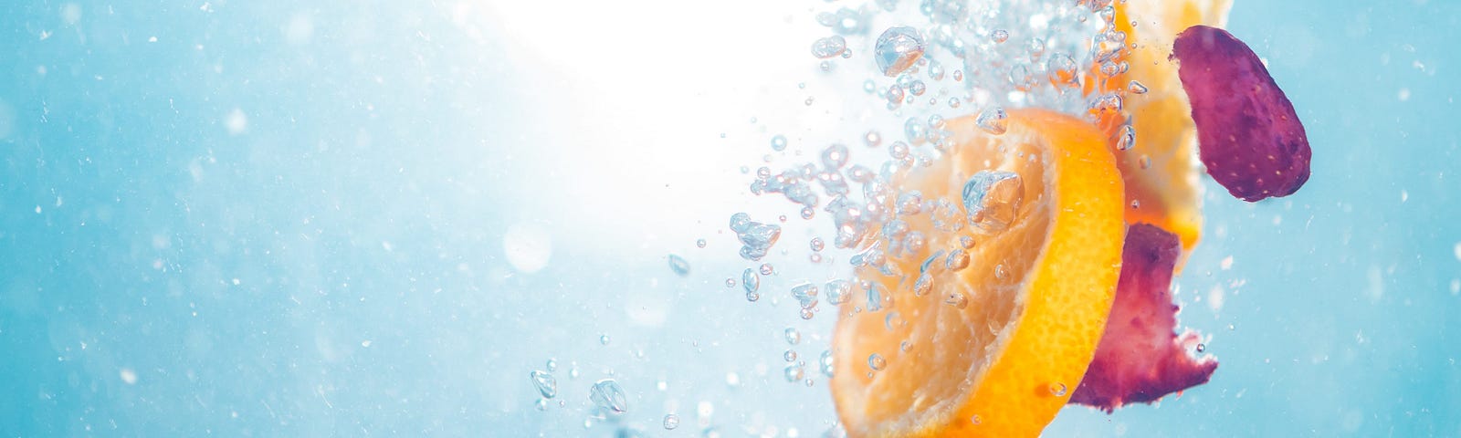 Slices of an orange and strawberries splashing into a glass of sparkling water.