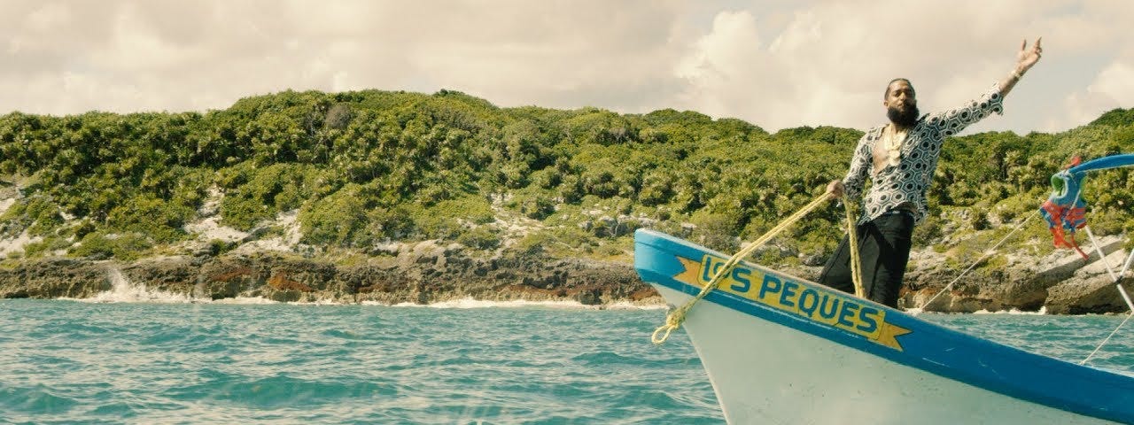 Nipsey Hussle on a boat with his left hand raised. A still from his music video for “Victory Lap”