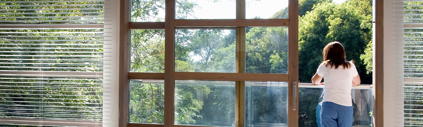 View through an empty room of a woman standing on a balcony.