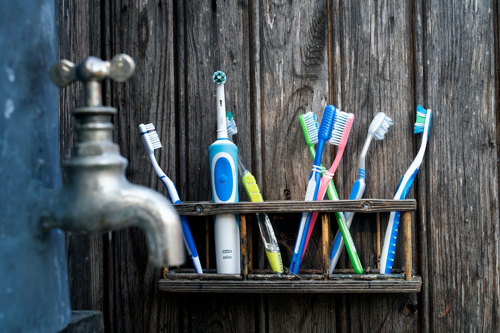 Multiple toothbrushes standing vertically on a wooden shelf next to an old-fashioned brushed chrome water faucet.
