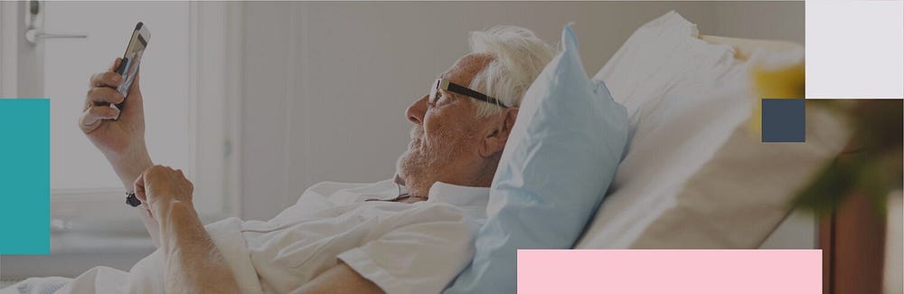 white haired man with glasses laying in hospital bed using FaceTime for Families program to communicate during Coronavirus
