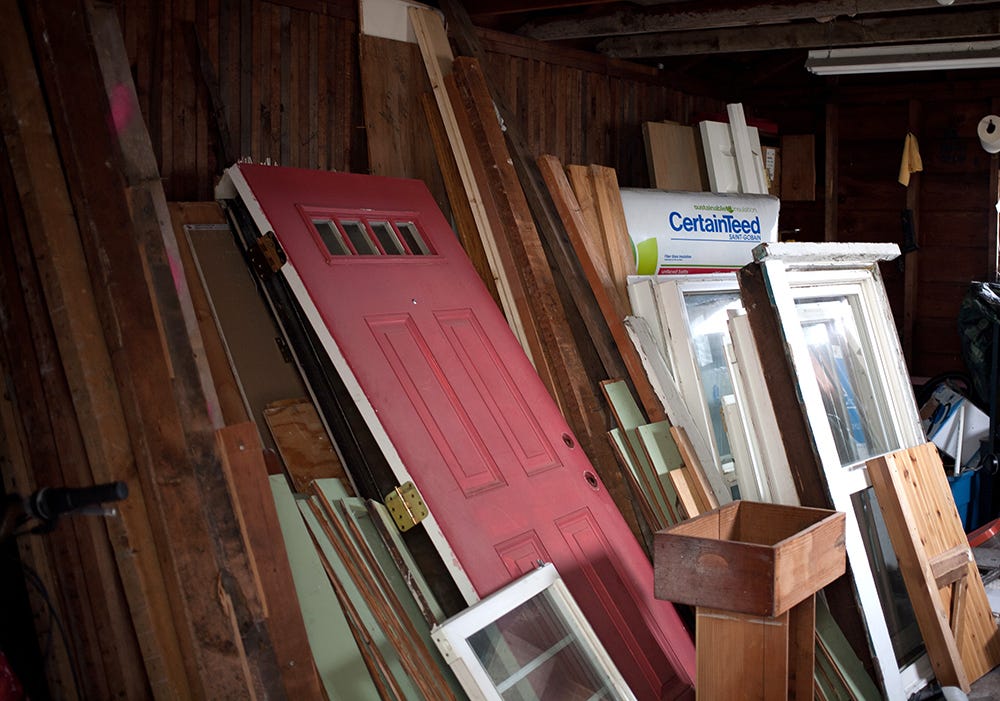 A red door, windows, and salvaged wood sit in a garage