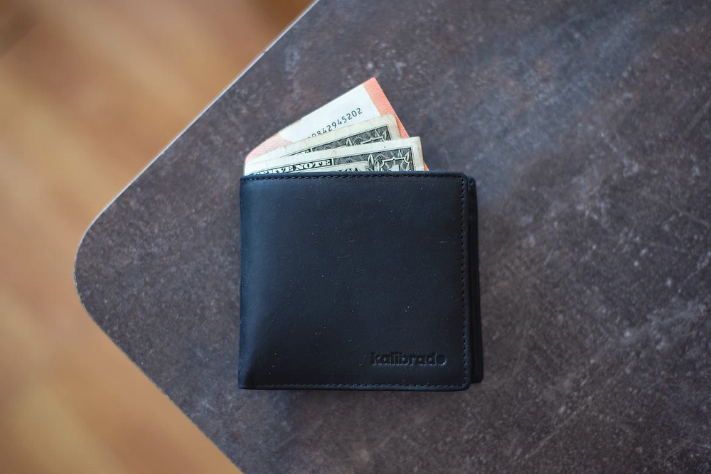 A folded black wallet with paper bills
