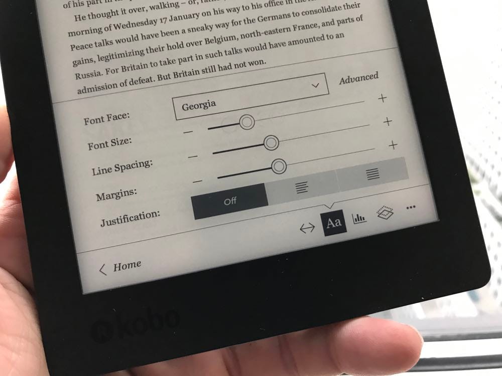 foto do leitor digital kobo segurado por uma mão branca, na tela aparece as configurações de texto (fonte, tamanho, espaçamento) e ao fundo o trecho de um livro