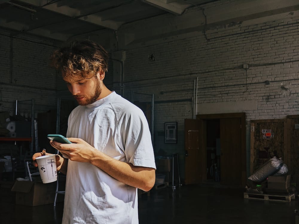 A young man is holding a paper cup while surfing social media on his phone. // onetoforseeforall/Pexels.