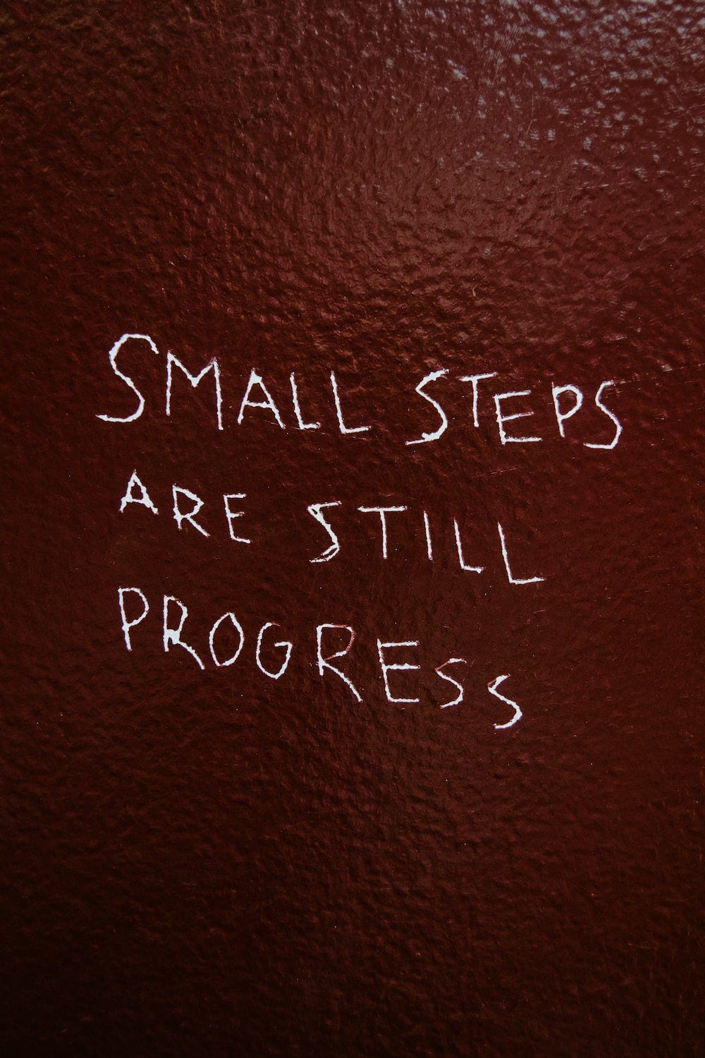 Charcoal writing on a wall about how small steps are still progress
