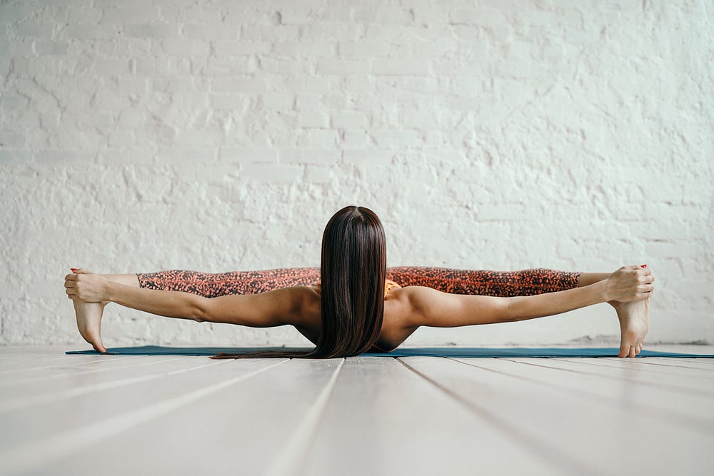 A woman stretching for legs far away from each other while lying on the floor.