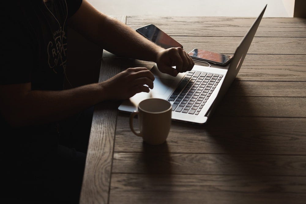 Person typing on a laptop at a wooden table with coffee and phone to the side