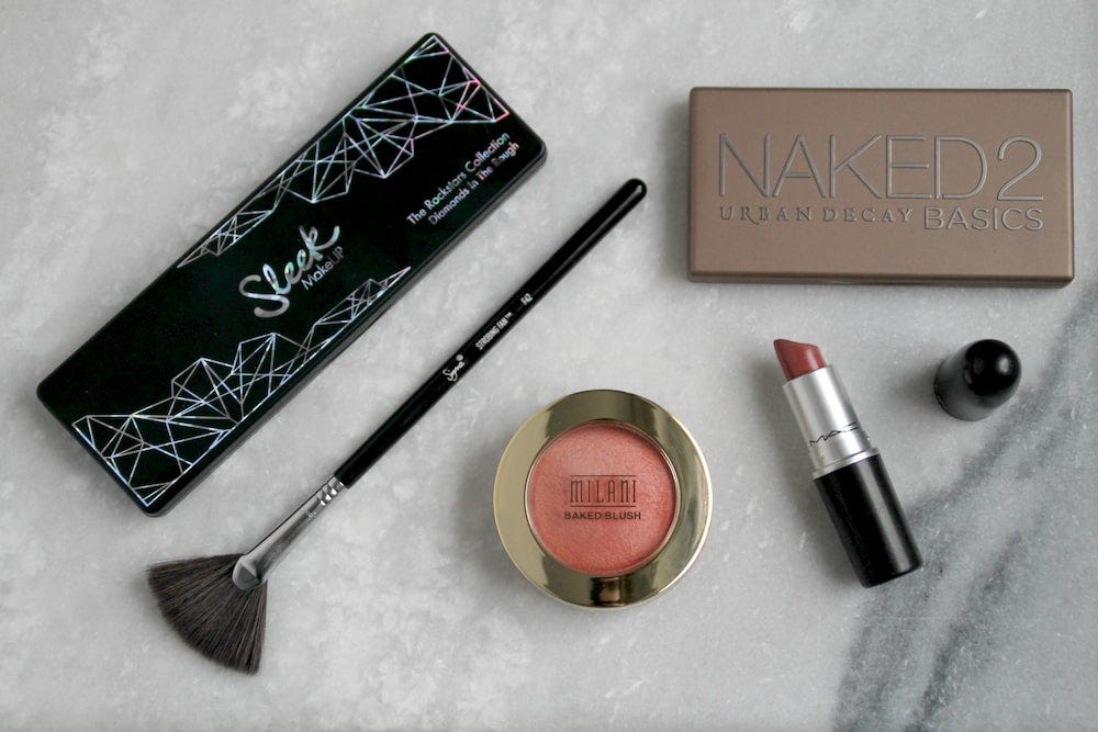Makeup on a marble background (from left to right: Eyeshadow palette, fluffy brush, blush, eyeshadow palette, lipstick)