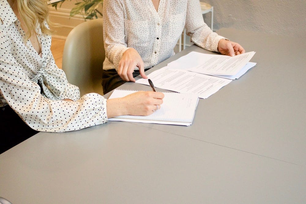 Two ladies sitting in the office discussing around some paper documents on the table.