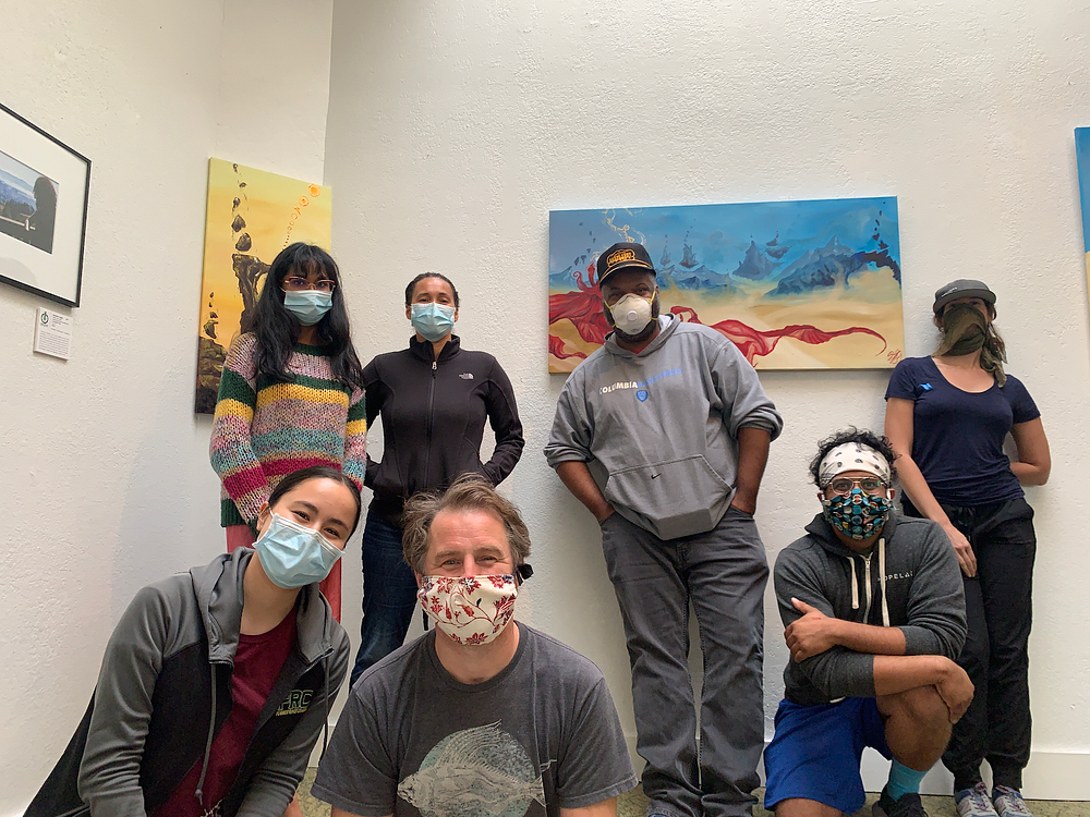 Seven figures standing in front of art on walls, all wearing face masks.
