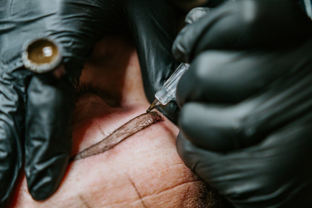 Tattoo artist tattooing eyebrows onto client