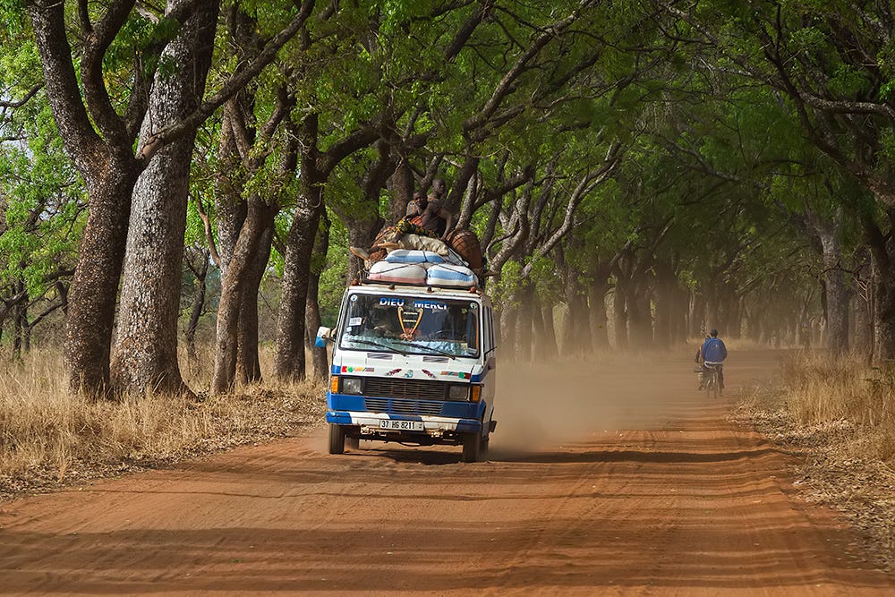 Un taxi-brousse circulando por una avenida de árboles en Banfora, Burkina Faso.