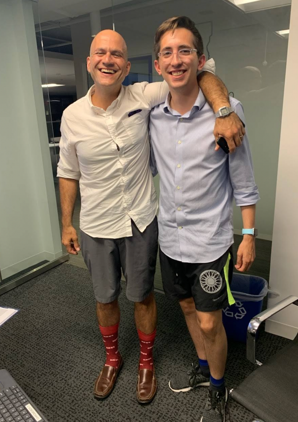 Doug Streat and Aledade CEO Farzad Mostashari wearing untucked collared shirts and shorts in a corporate office.