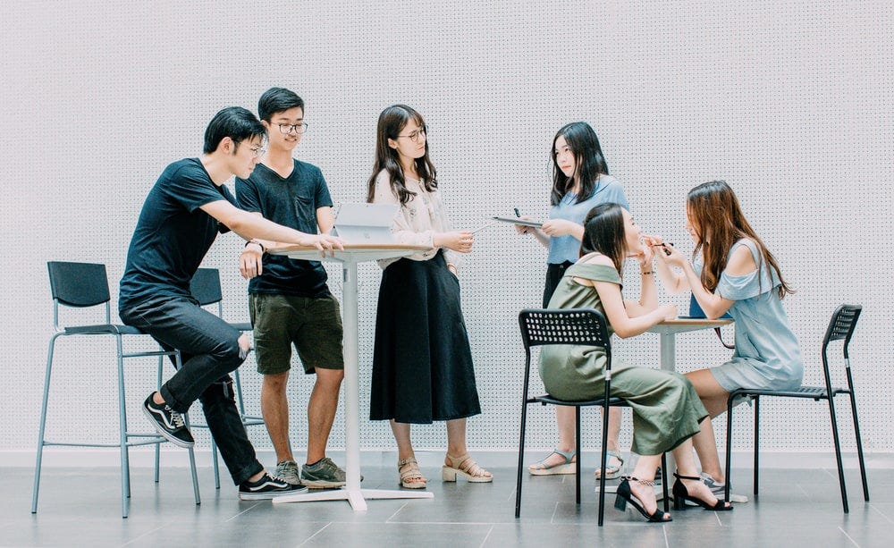 Young group of students milling about talking about a project.