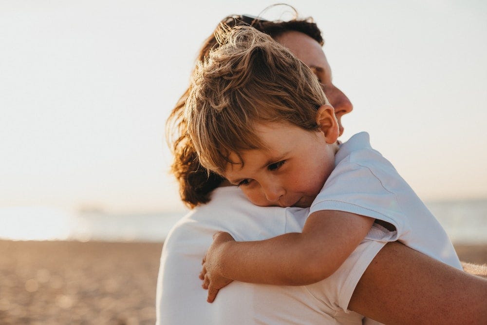 A kid hugging his mother, both wearing white t-shirts.