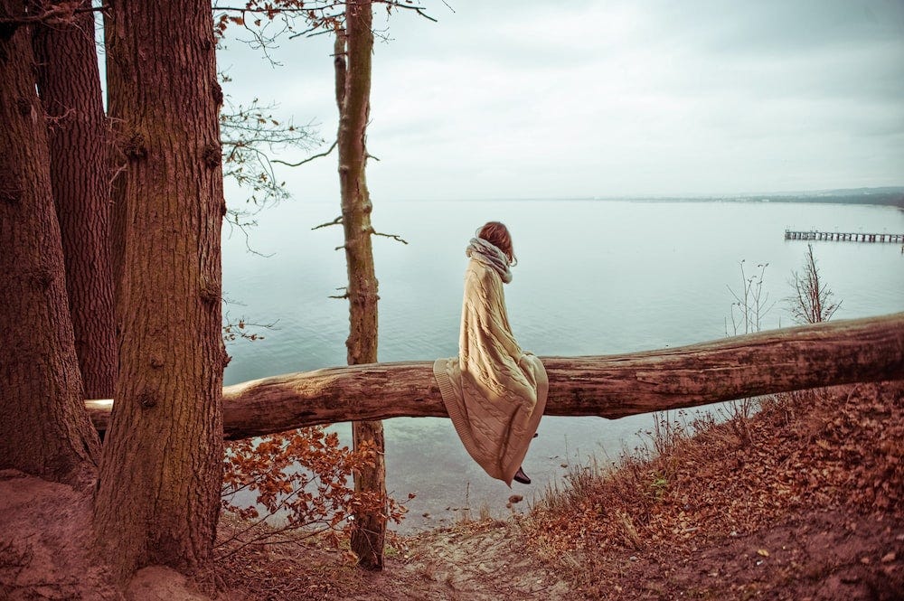 A woman is sitting on a tree log near the sea. Pawel Szvmanski/Unsplash.