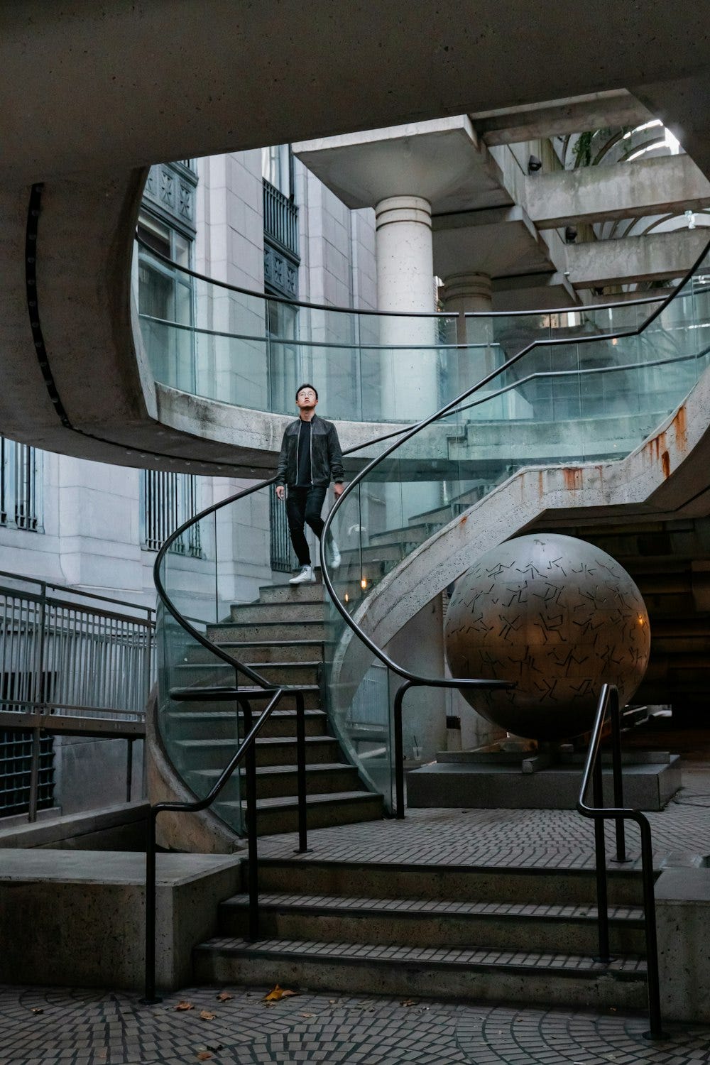 Descending a spiral staircase, a man is accompanied by a captivating circular globe embedded in the ground to the right as he reaches the end of the stairwell.