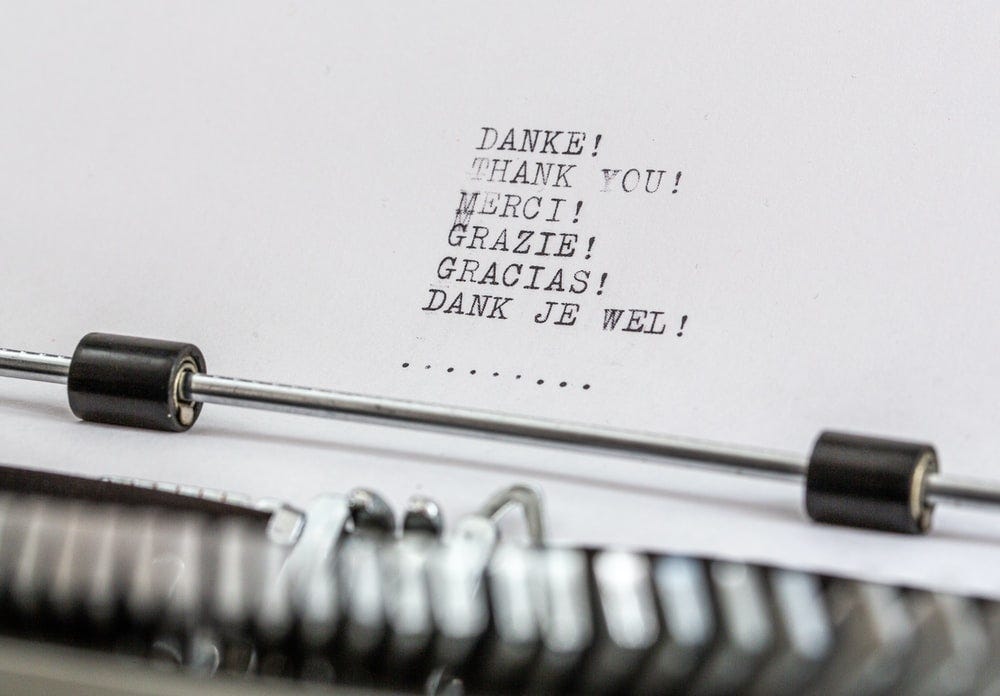 A close up of a typewriter with the words “thank you” written in multiple languages