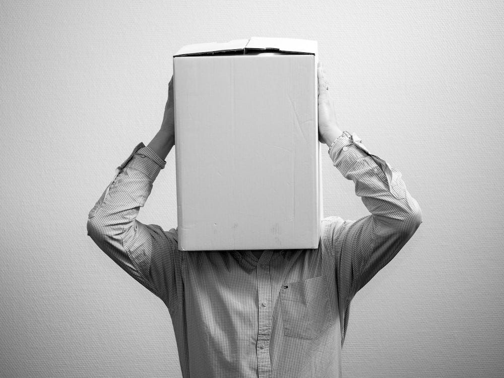 A man holding a box over his head and covering his face.