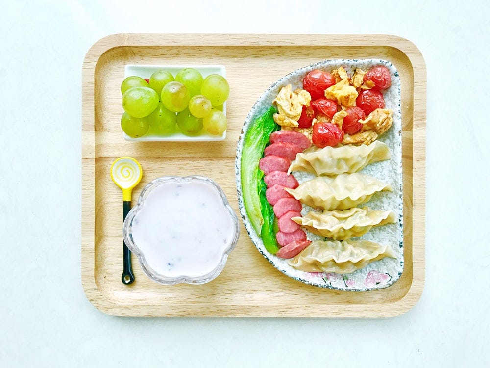 A plate containing bowl of grapes, curd, spoon and a meal.