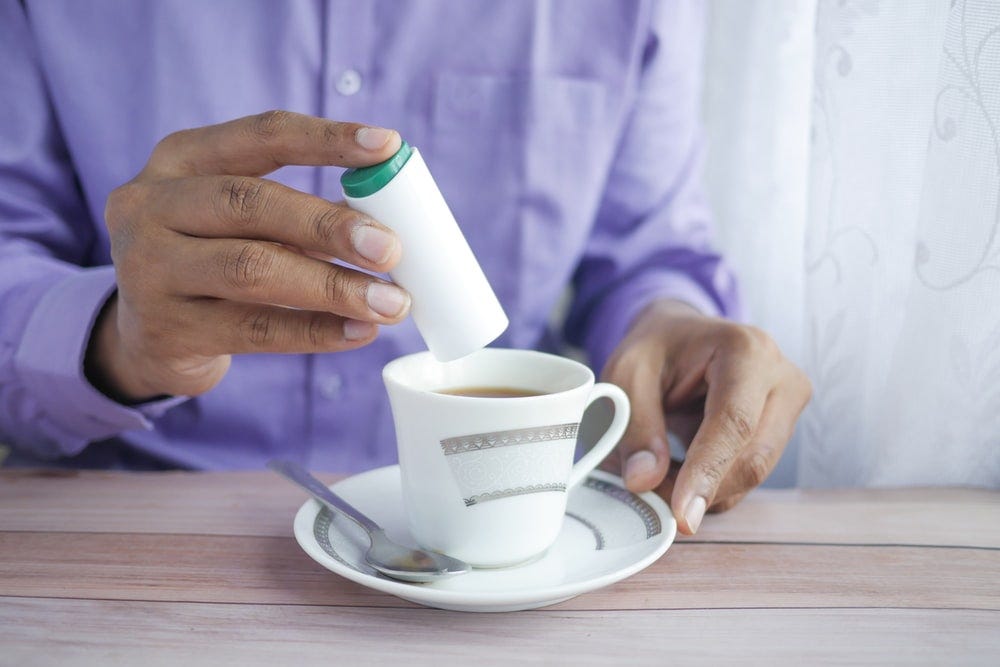 A man adding artifical sweetener to a cup of tea.
