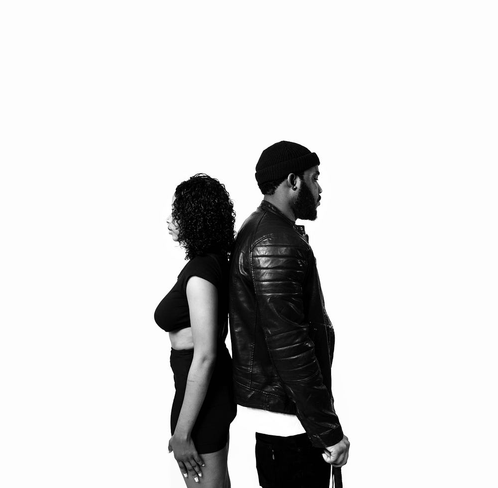 A black and white image of a Black couple standing back to back.