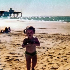 Baby at the beach with wet pigtails and a green bikini.