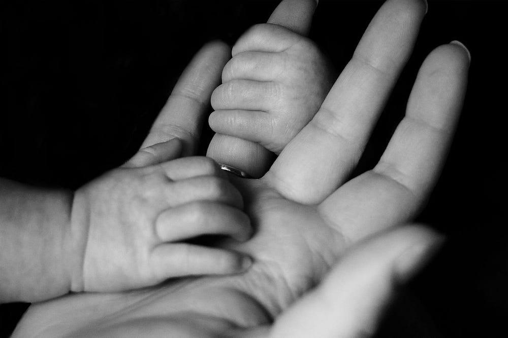 A tiny infant hand clasping the much larger hand of a parent.